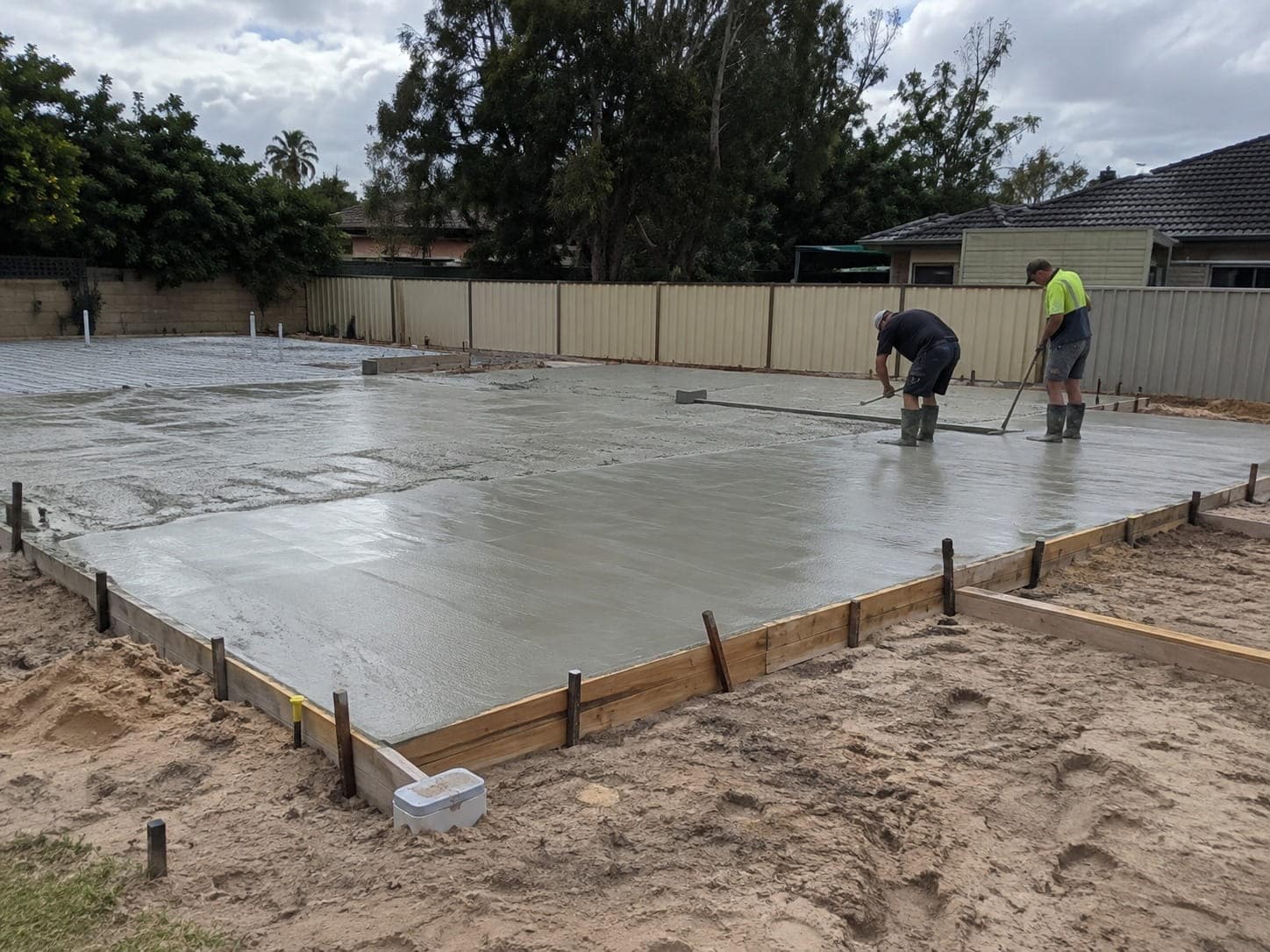 Two concreters screeding a freshly poured house slab inside timber formwork
