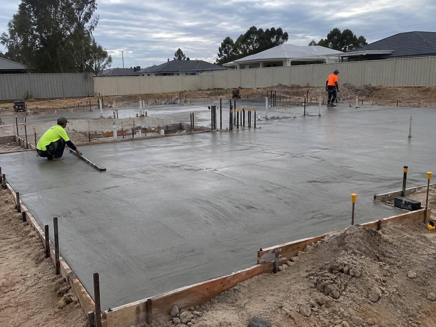 Two concreters finishing a freshly poured house slab