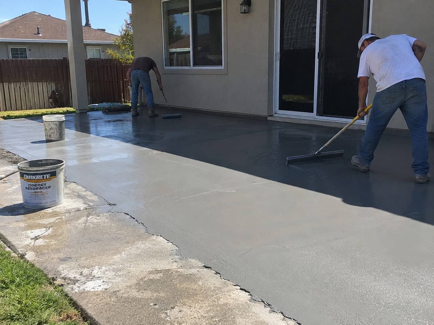 Workers spreading a fresh overlay across a worn patio