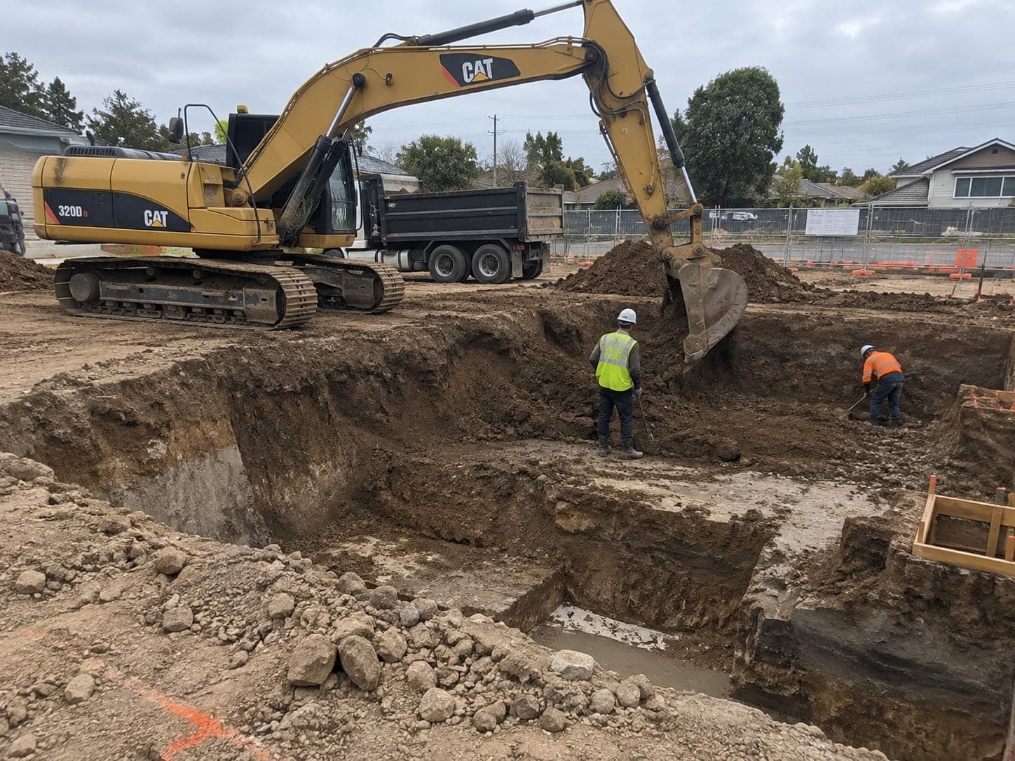 Excavator cutting a deep bulk excavation with workers trimming the base