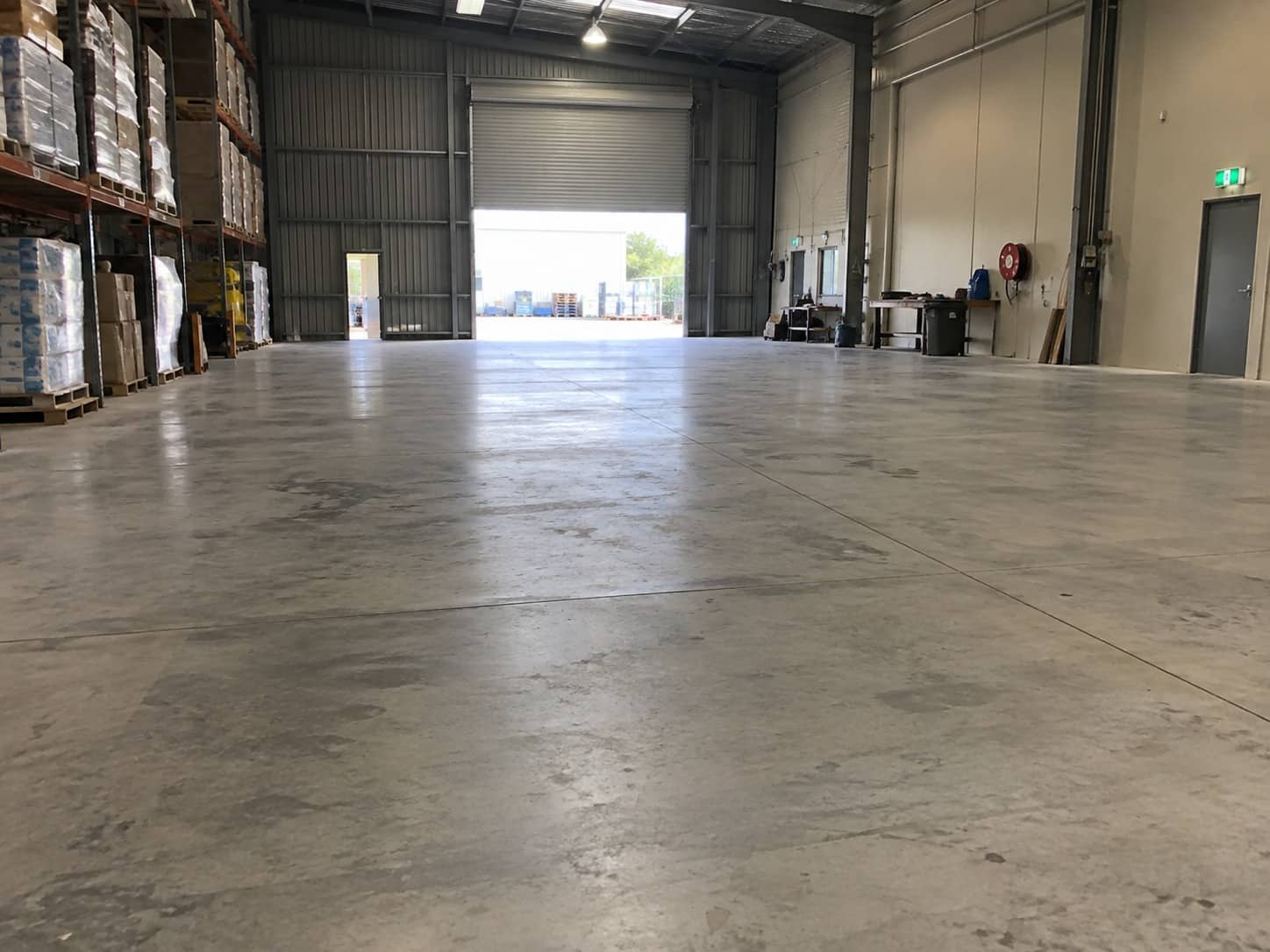 Wide industrial concrete floor inside a Mandurah warehouse, pallet racking along one wall and the roller door open at the far end