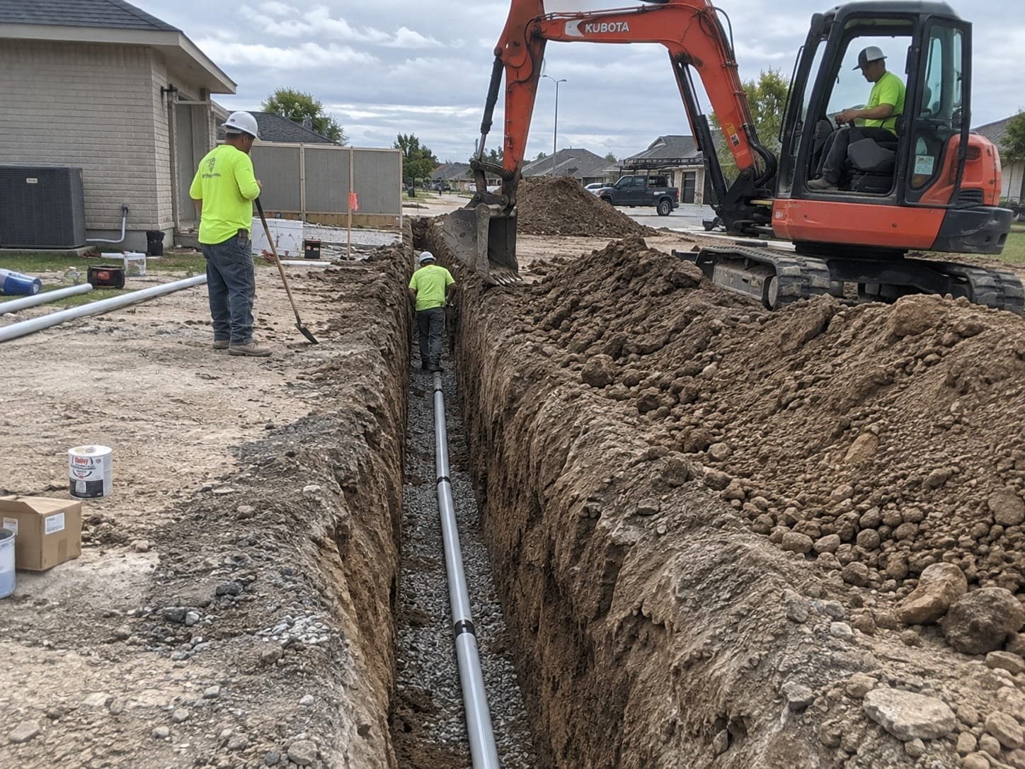 Open trench with pipe laid on a gravel bed and an excavator alongside